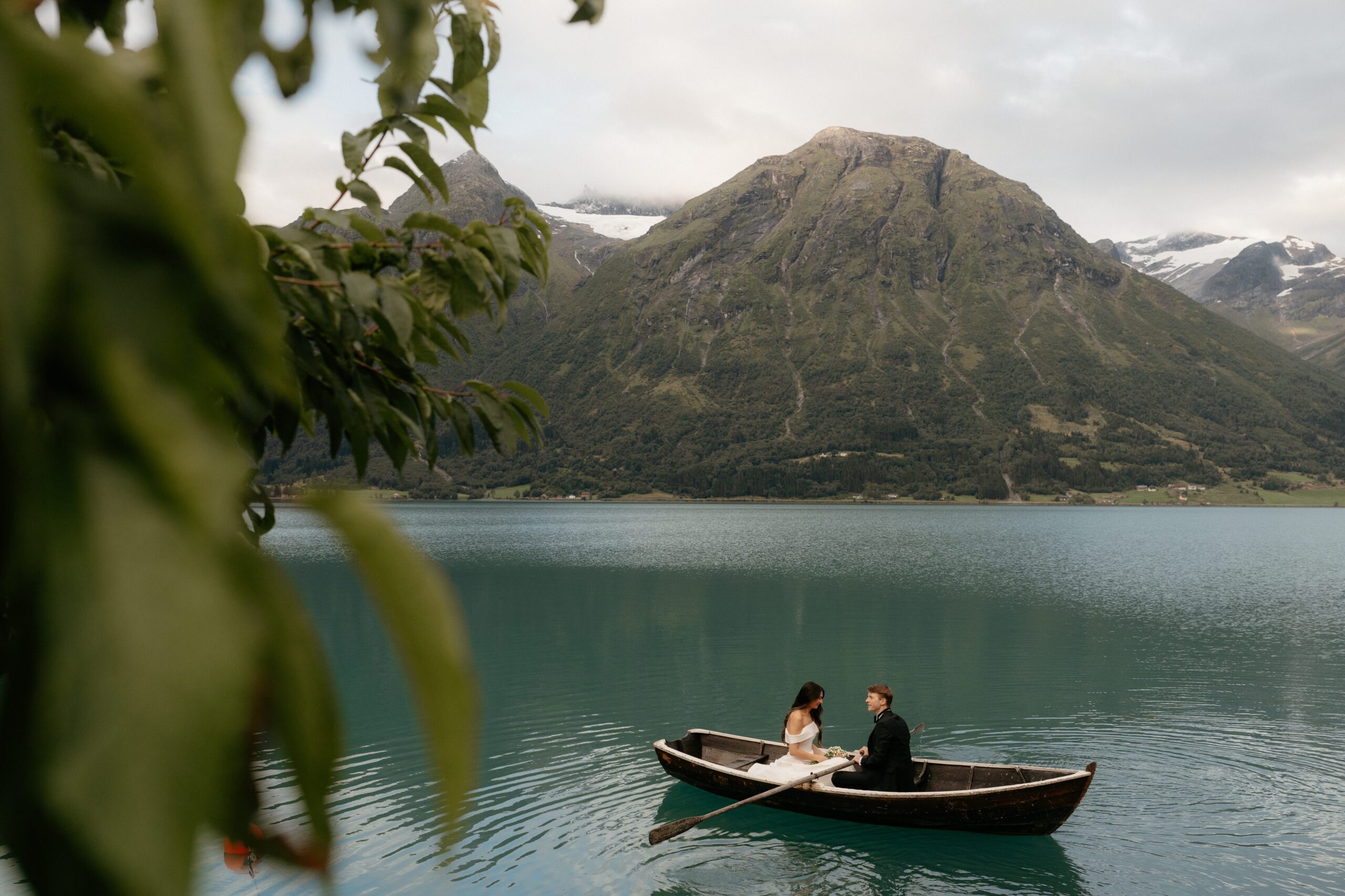 Couple rowing a wooden boat on a glacier lake in Hjelle, Norway at sunrise.